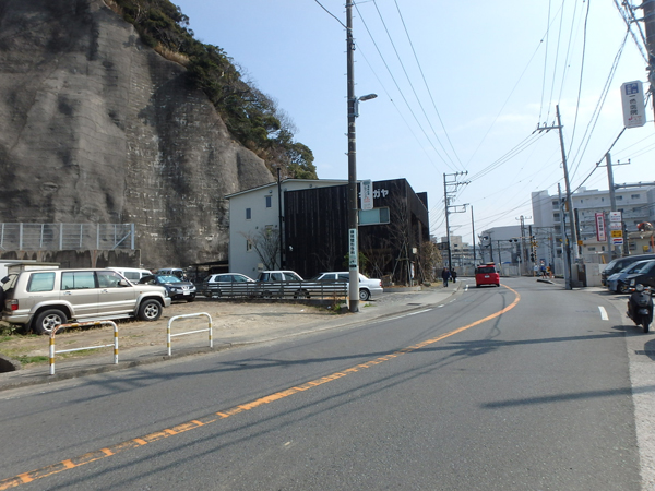 前面道路。左側の駐車場になっている場所が当土地です。この写真を見てピンと来るかたも多いはず。