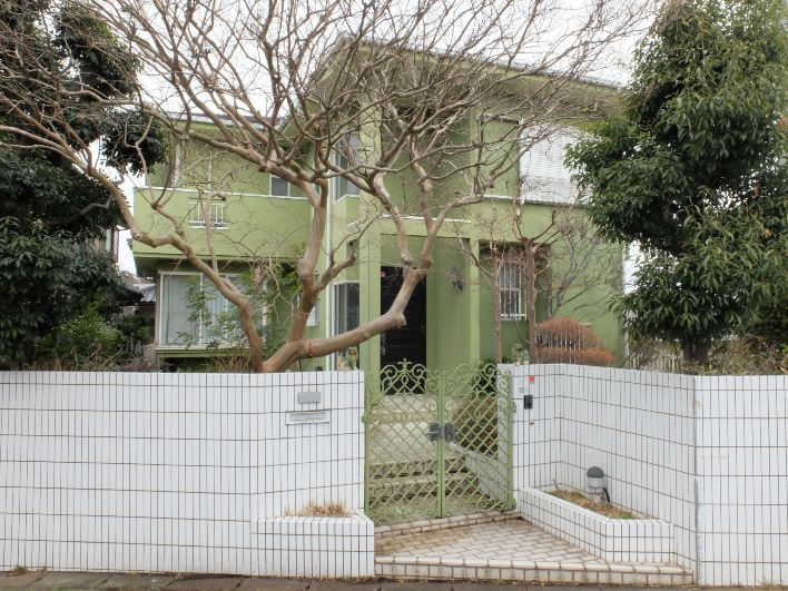 白いタイルに緑の外観。大きく枝を伸ばすサルスベリの開花が待ち遠しい。